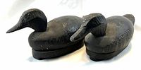 Side view of two dark carved pine antique duck decoys positioned side by side on a white surface.