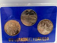Obverse of three coins showing flag-raising, industrial and dove/tower designs against blue insert