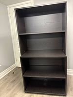 Front view of black-brown IKEA bookshelf with four shelves, including one adjustable shelf.