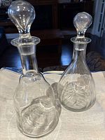 Front view of two clear glass decanters with stoppers, showing overall shape and size difference.