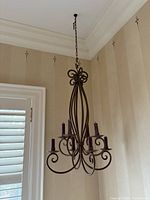 Photo of iron 8-candle chandelier candelabra hanging from ceiling showing full vertical design, chain and candle holders.