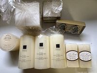 Nine unopened candles and candle boxes shown on white surface, including pillar candles and decorative boxed candles.