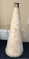 Full view of the antique megaphone showing its tall, tapered conical shape with textured, cracked white surface and faint inscriptions.