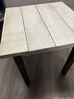 Top view showing rustic creamy milk-wash wooden planks and wood grain on a four-plank rectangular tabletop with a dark brown leg edge partially visible.