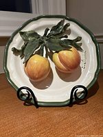 Front photo of the ceramic plate with 3D peaches on green-rimmed white base with stand.
