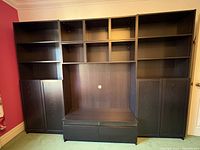 Photo shows the closed bookcase and TV stand unit in black-brown wood finish with open shelving above and enclosed shelving with doors below on each side and two drawers at the bottom center.