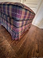 Close-up of the side and fabric pattern of the ottoman, showing plaid upholstery with diamond accents and skirt detail.