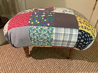Side view of patchwork footstool showing colorful fabric patches and turned wooden legs on carpeted floor.
