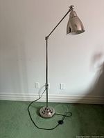 Full view of silver floor lamp showing adjustable arm and lampshade with silver finish.