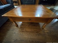 Front view of the square wooden coffee table showing the top surface, one drawer with a round knob and turned legs.