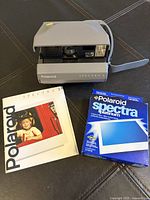 Polaroid Spectra 2 camera with instruction booklet and unopened pack of Spectra Platinum film arranged on a dark surface