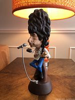 Full view of Bob Dylan caricature ceramic figurine sitting on brown base, holding guitar and harmonica with microphone stand in front.
