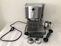 Full view of Breville espresso machine with accessories arranged around it: portafilter, two filter baskets, coffee scoop and tamper, stainless steel frothing jug, power cord visible.