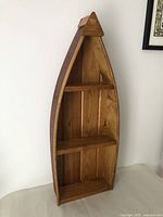 Front angle view of wooden canoe shelf showing three interior shelves and rounded pointed top.