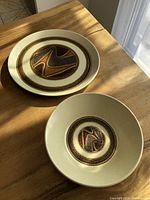 Set of a platter and bowl shown on wooden table with natural light, highlighting the circular abstract landscape design in brown and rust.