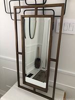 Full view of rectangular bevelled mirror with metal frame showing Ming style open work design, mounted on wall vertically near light switches.