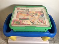 Green plastic Lego Dacta 9651 case with clear lid showing instruction artwork, placed on blue and yellow Lego table.