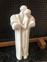 Full view of white/cream stone sculpture showing two figures in an abstract embrace with flowing form around their shoulders.