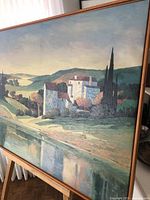 Close-up side angle showing framed screen print on canvas with scenic landscape and large buildings in the foreground.