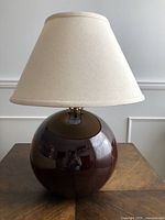 Full view of the lamp showing the round brown ceramic base and cream fabric shade.