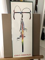 Full view of the vintage John D. Wibberley bicycle print in original packaging, showing the top-down colorful bicycle design with green border and red signature text.