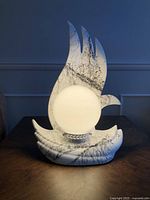 Front view of the white ceramic flame-shaped lamp with central spherical light glowing, showing black veining on the flame-shaped ceramic base and back drops, placed on dark wooden surface.