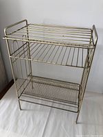 Front angle view of vintage gold tone metal turntable and vinyl record stand showing construction and shelf design.