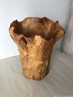 Wood burl vase showing natural, irregular wavy edges and light to medium brown finish with visible grain patterns and texture, photographed from front angle.