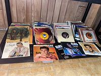 Photo showing a collection of 45 rpm vinyl records with various paper sleeves, featuring artists like Ricky Nelson, Elvis Presley, and others, arranged on a wooden floor.