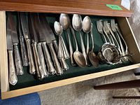 Felt-lined wooden drawer showing full set of knives, spoons, forks and silver serving pieces.