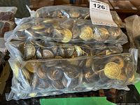 Eleven vacuum-sealed bags filled with gold-colored coat buttons stacked on a table.