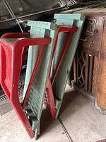 Two metal car ramps with red painted perforated metal ramps mounted on teal painted wooden bases, leaning against a wall in a garage.