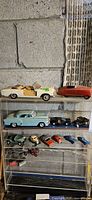 Full view of toy car collection on cracked shelf showing multiple toy cars including vintage and smaller scale models.