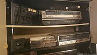 Multiple shelves containing electronic audio and video devices: mixer, Betacord, Toshiba player, Sony radio tape player.