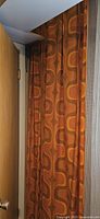 Two vertically hanging drape panels with geometric retro pattern in a corner near a door.