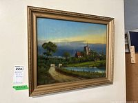 Full view of the framed reverse on glass painting, showing the countryside scene including church, pond, path, and bridge.