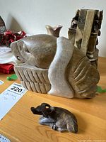 Photo showing the large carved stone figure of an eagle with a man wrapped around it, along with the small carved ox figure on a wooden surface.
