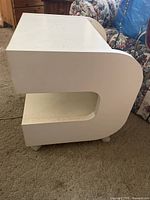 Side view of white laminate side table showing curved side panel and middle shelf