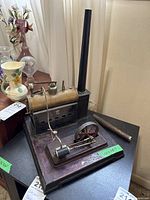 Front view of entire steam engine on wooden base with attached chimney and extra chimney beside it