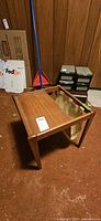 Teak side table with fabric magazine holder attached on one side in basement setting. Visible scratches and wear present on the table surface.