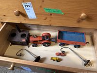 Drawer with vintage toy tractor, trailer, miniature stove, two metal lamp stands with bulbs, and two small toy vehicles.