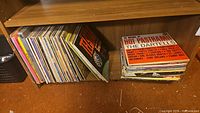 Shelf view showing around 30 vinyl records stacked mostly vertically with various colorful album covers visible.