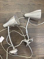 Two silver metal clip-on lamps laying on a wooden surface, showing clip bases and cords.
