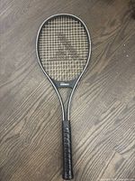 Full tennis racket showing black frame, strings, and wrapped grip