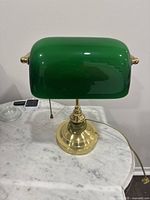 Front view of the vintage green glass banker desk lamp with brass base showing the curved shade and pull chain.