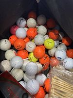 Inside view of canvas bag containing used golf balls in white, orange, yellow, and pink colors along with bags of wooden tees.
