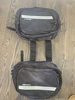 Two connected black Sidewind motorcycle bags with reflective silver stripes and multiple compartments laid on a wooden floor.