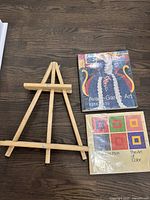 Wooden tabletop easel alongside two art books on a dark wooden surface.