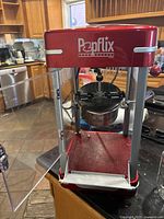 Full view of the popcorn machine showing the red Popflix label on the top and the clear door open to reveal the kettle inside.