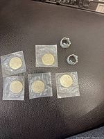 Seven uncirculated nickel commemorative coins labeled 'Rodeo East 81' each sealed individually in plastic sleeves on a leather surface.